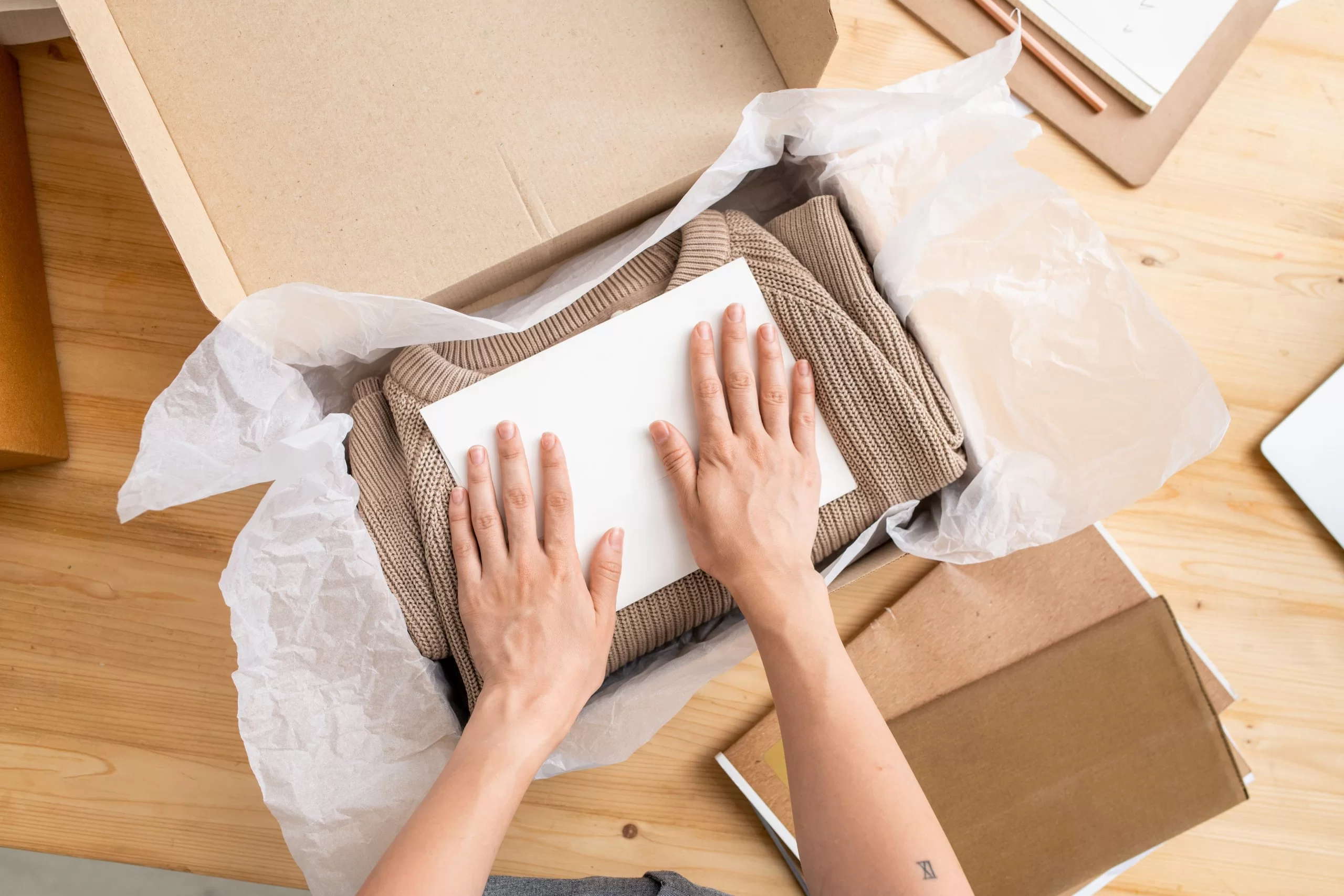 hands putting paper on top of folded sweater in box