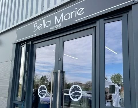 The exterior of a store named "Bella Marie Apparel" featuring large glass doors. The sign above the entrance displays the store name in white letters against a dark background.